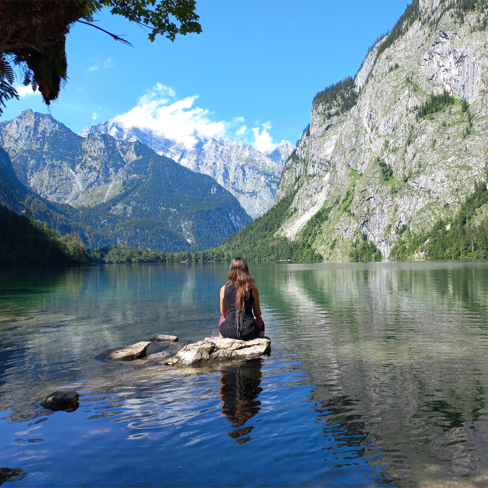 Eine Frau sitzt auf einem Stein in einem Bergsee